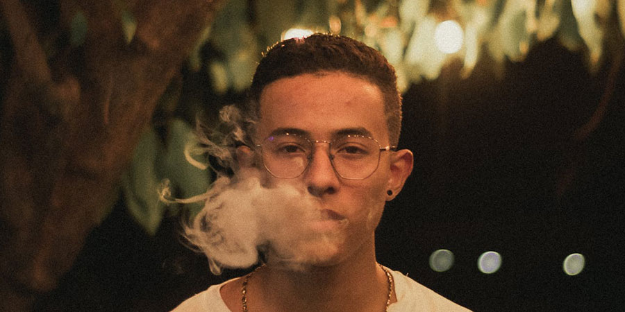 a man with glasses vaping outdoors during night time